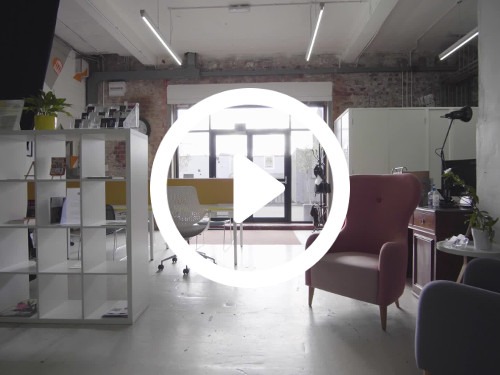Contemporary workspace featuring pink coloured traditional armchair next to modern white bookcase in front of large windows Google Meet background