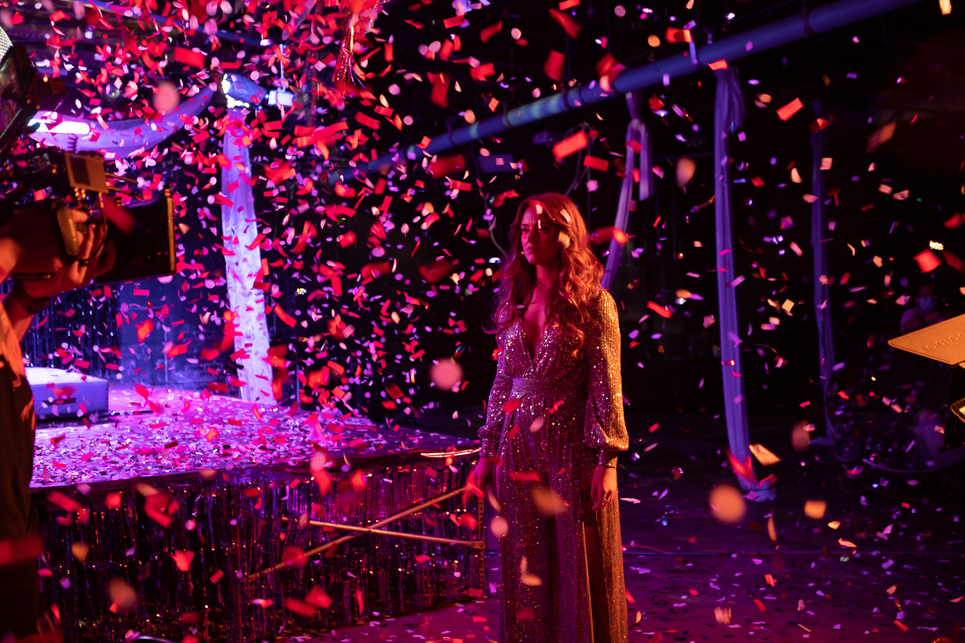 A woman in a shimmering dress standing alone in the confetti. 