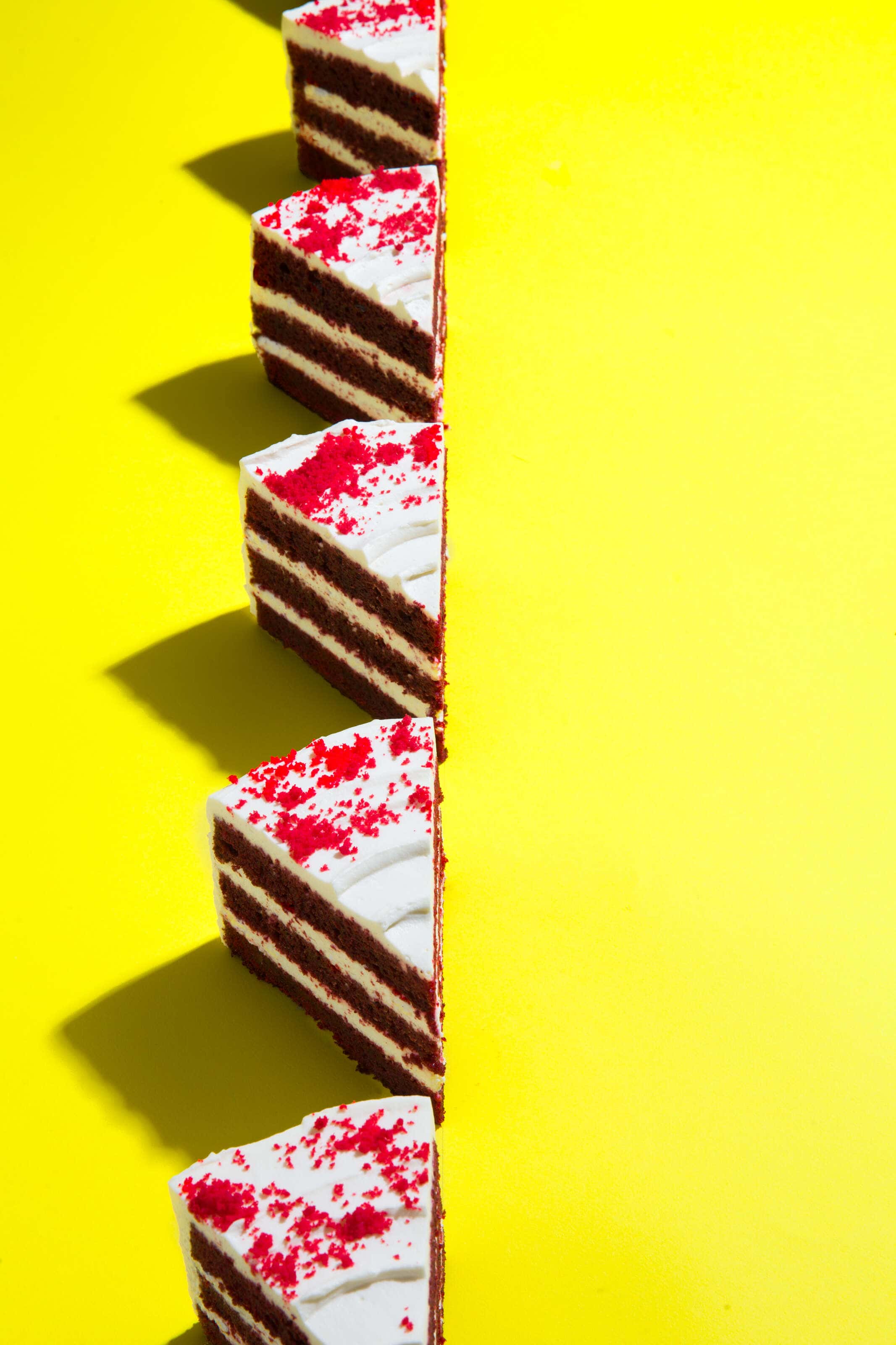 Red velvet cake photographed on a yellow background with hard shadows in a pop art style.
