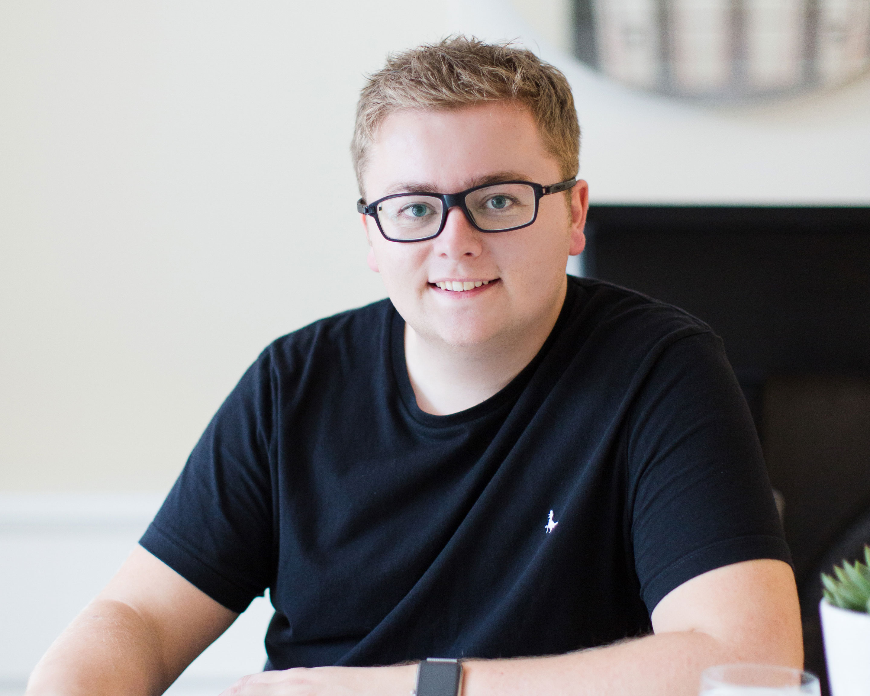 Jack Watkins in black glasses and black t-shirt smiling at the camera