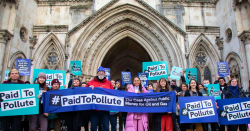 A mixed group of people standing in front of the royal court of justice, holding paid to pollute banners and placards