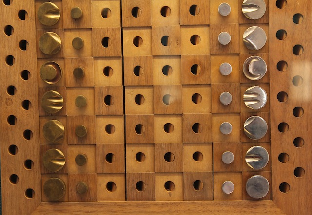 a wood and brass chess set, where squares have peg holes for each playing piece, and each brass unit has distinctive markings on top.