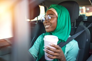 Young African Muslim woman driving a car. Muslim woman driving car, and enjoys it. Smiling black muslim woman driving her vehicle and drinking coffee to go. Arab Women Driving Car routine STI STD testing Nigeria