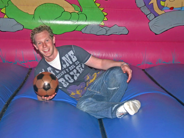 A single male adult sitting on a bounce house with a soccer ball