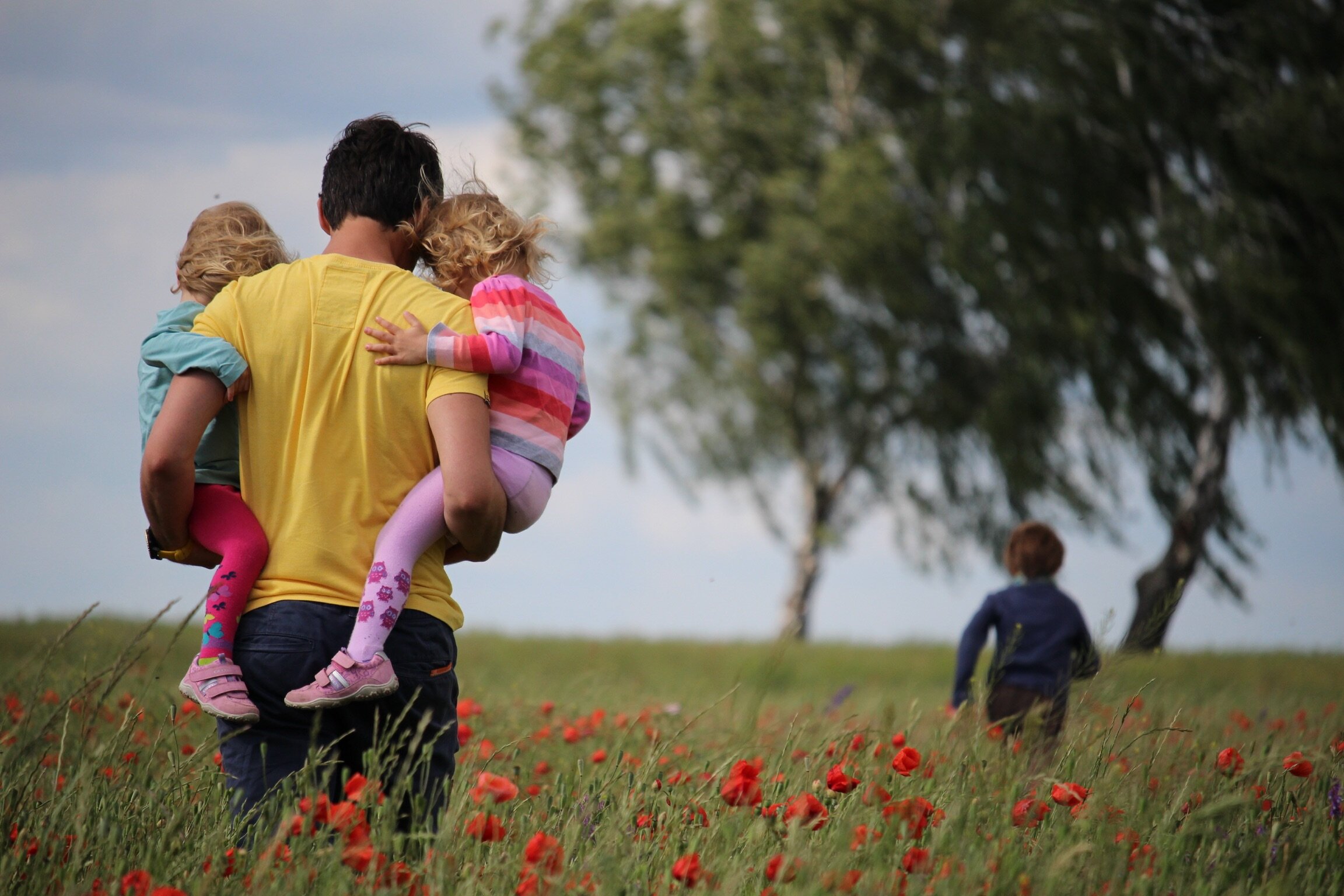 A man is carrying his kids through a field of grass