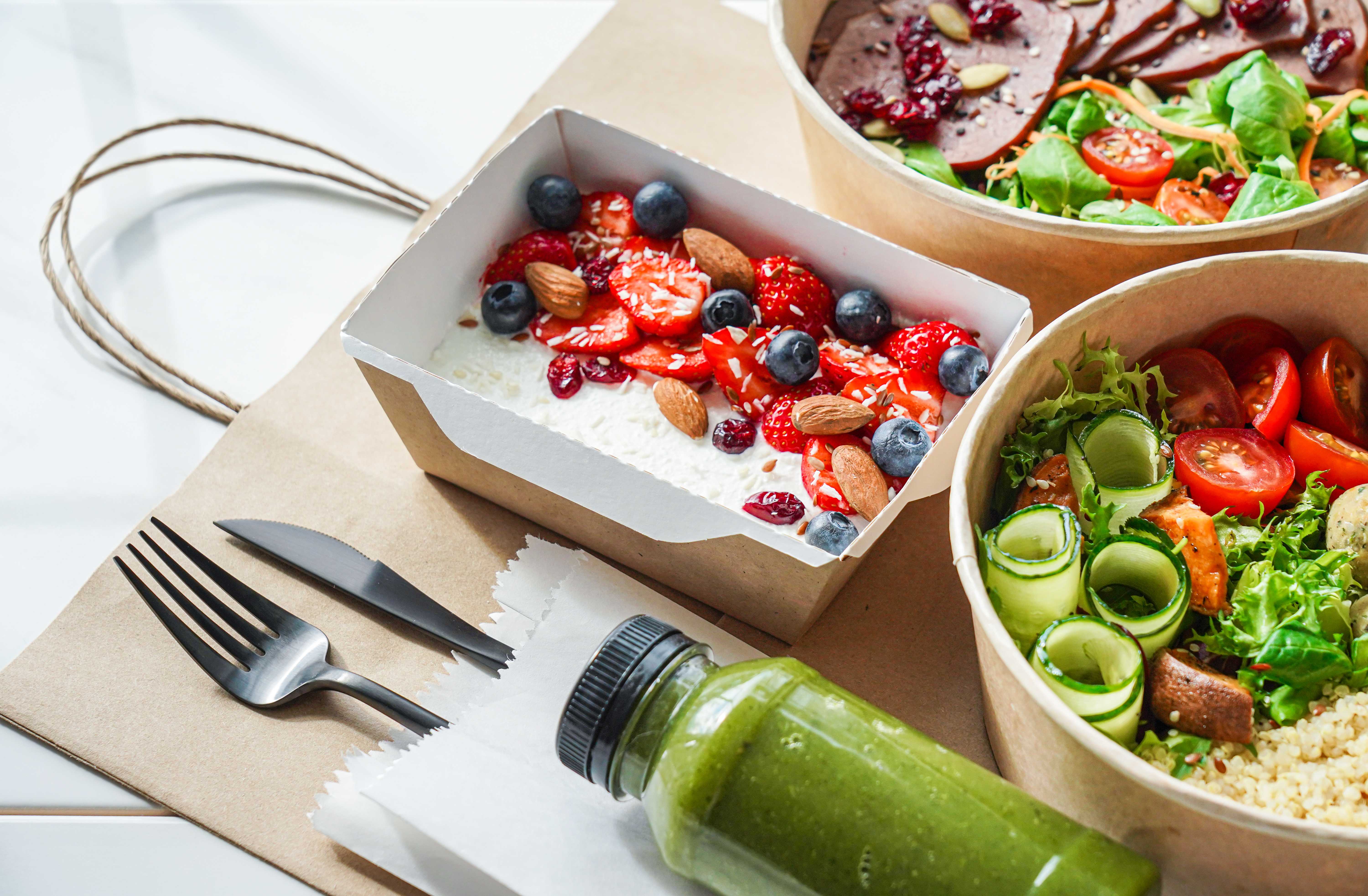 Refreshing takeout food; yogurt, grain bowl, salad, and green juice. Disposable takeout containers, utensils, and paper bag.