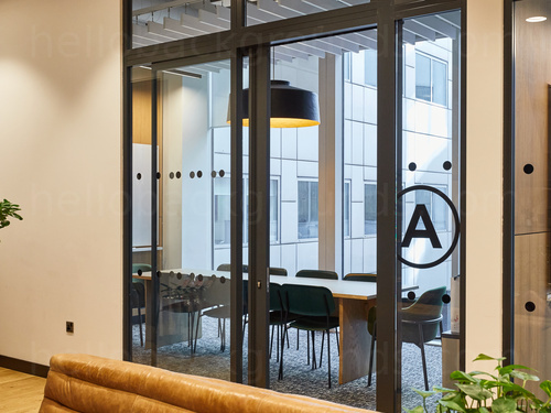 Compact boardroom with large interior and exterior windows containing long wooden table and black chairs Zoom background
