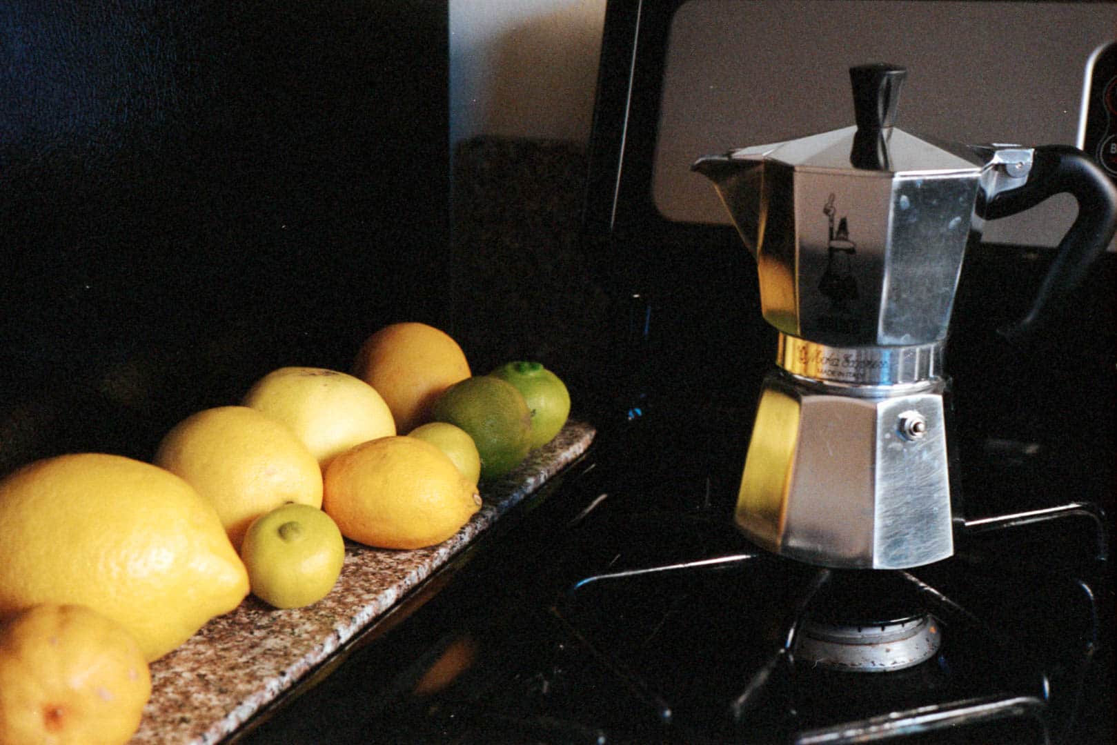 Lemons lined up alongside a stove with a coffee maker