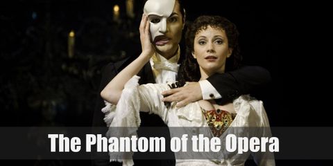 The Phantom wears a dapper costume consisting of a white dress shirt, black vest, black coat, black dress pants, black Oxfords, white gloves, black cape, and a personalized white half-mask.