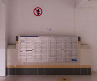 A no littering sign on the bare concrete wall of a HDB void deck in Yishun. Rows of metal letterboxes are installed under the sign.