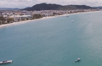 Foto aerea do mar de Canasvieiras com alguns barcos navegando e faixa de areia bem ao fundo.