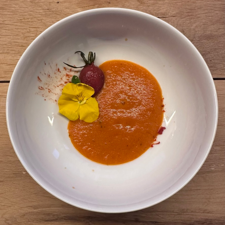 a bowl with tomatoes roasted, sauced, and souped, with a voilet garnish
