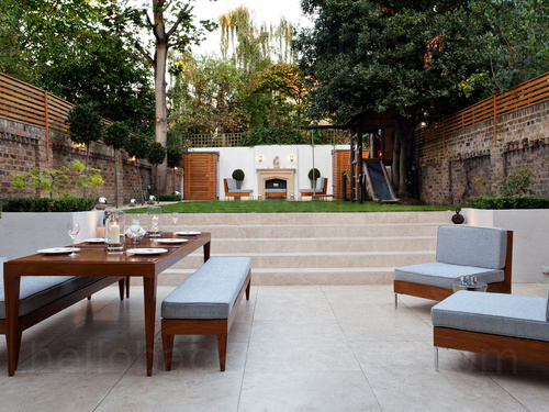 Modern garden dining area featuring wooden furniture decorated with light blue upholstery in front of a well kept lawn  Google Meet background