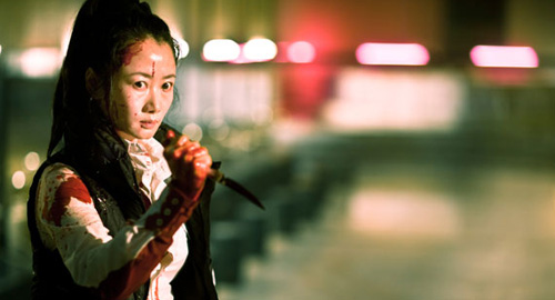 A screenshot from the film 'A Touch of Sin' of Xiaoyu (played by Zhao Tao) holding a bloody knife while staring intently at the camera.