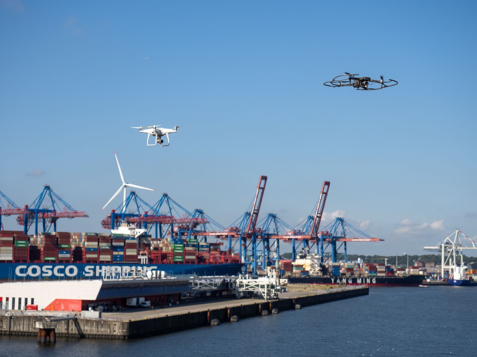 Two drones flying over containers in a cargo port.