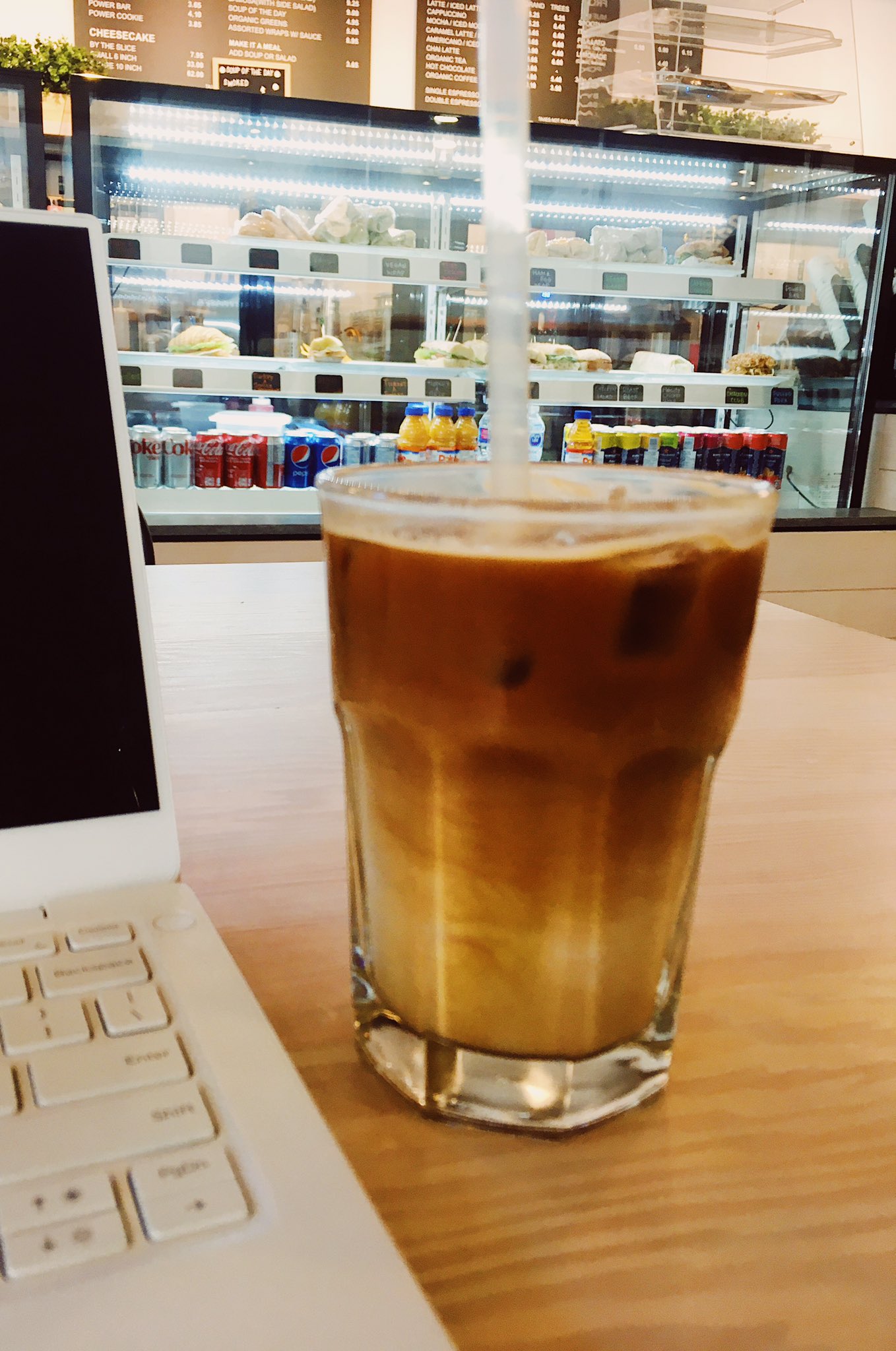 A slightly blurry iced latte next to my laptop at a cafe.