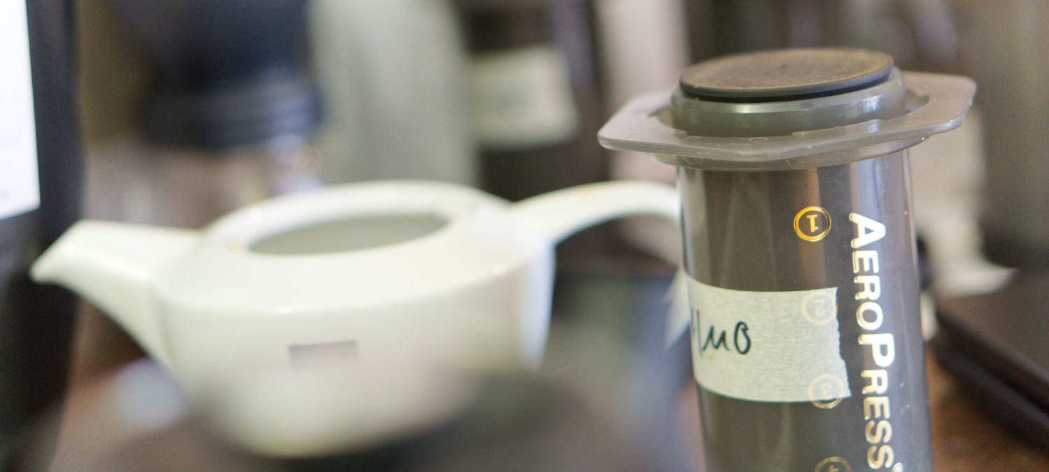 An aeropress coffee maker in front of a tea pot
