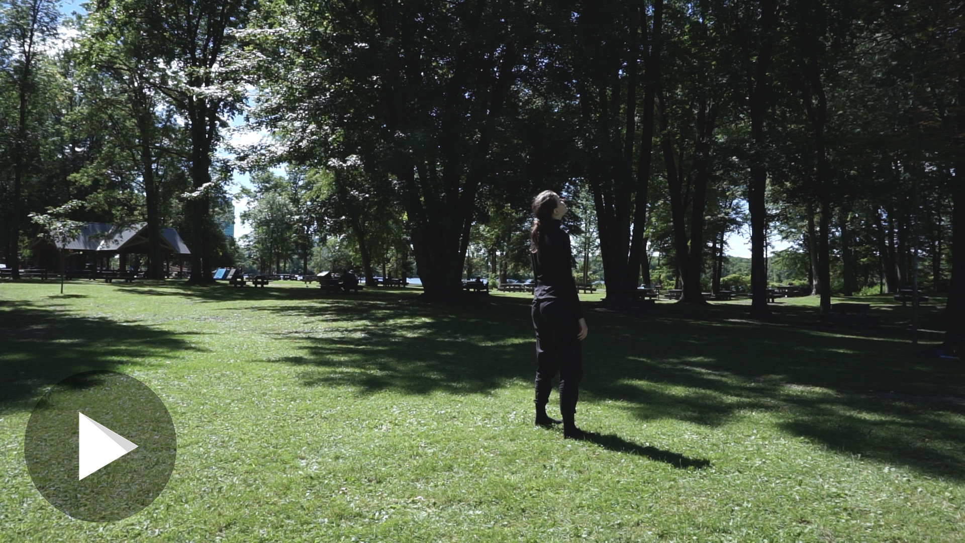 Clara debout regardant au loin, dans un parc; symbole PLAY en bas