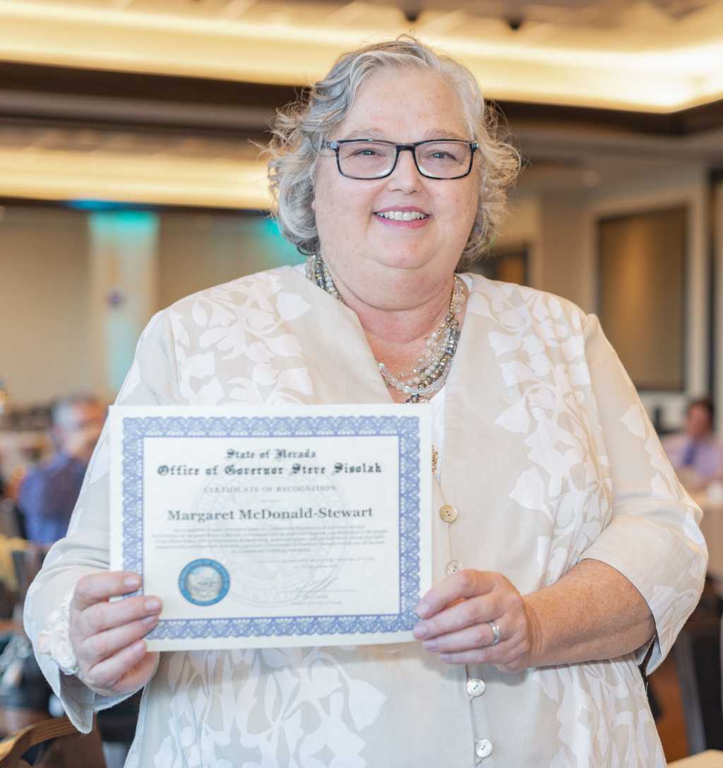 Margaret Stewart stands, holding the Governor's certificate of achievement.