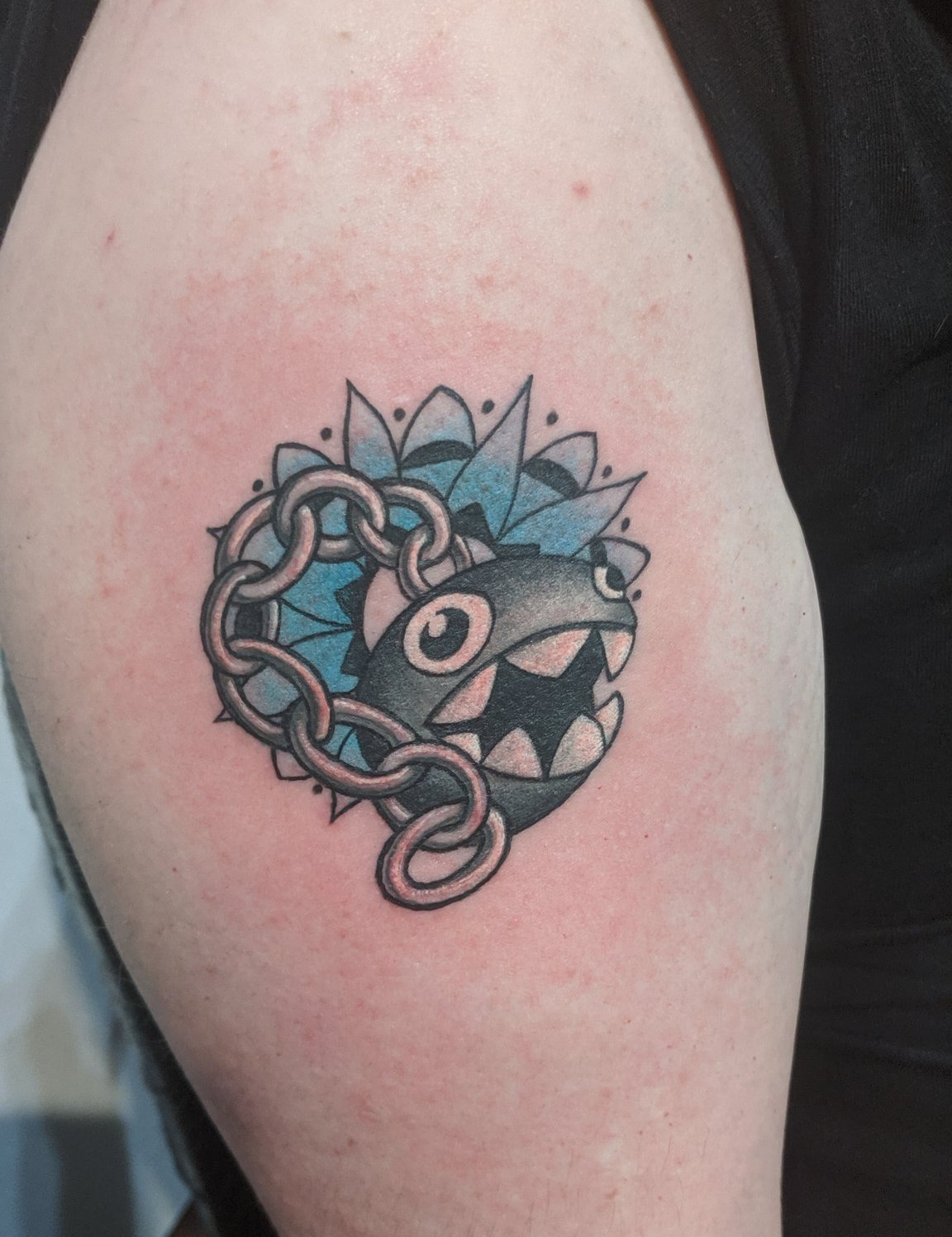 A photo of Squidge’s tattoo, located on his upper right arm. The tattoo consists of a chain-chomp from the Super Mario universe,on an explosive teal background.