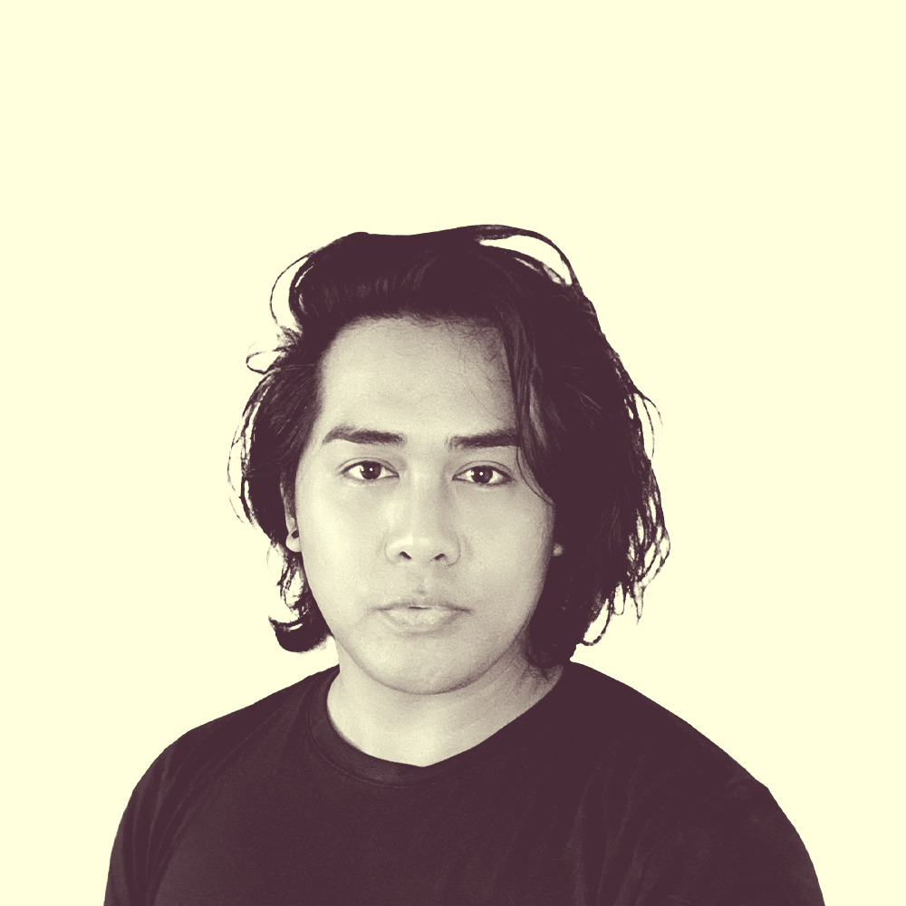 A Filipino-American male with long hair. He is facing the camera, lightly grinning, and is wearing a black shirt.