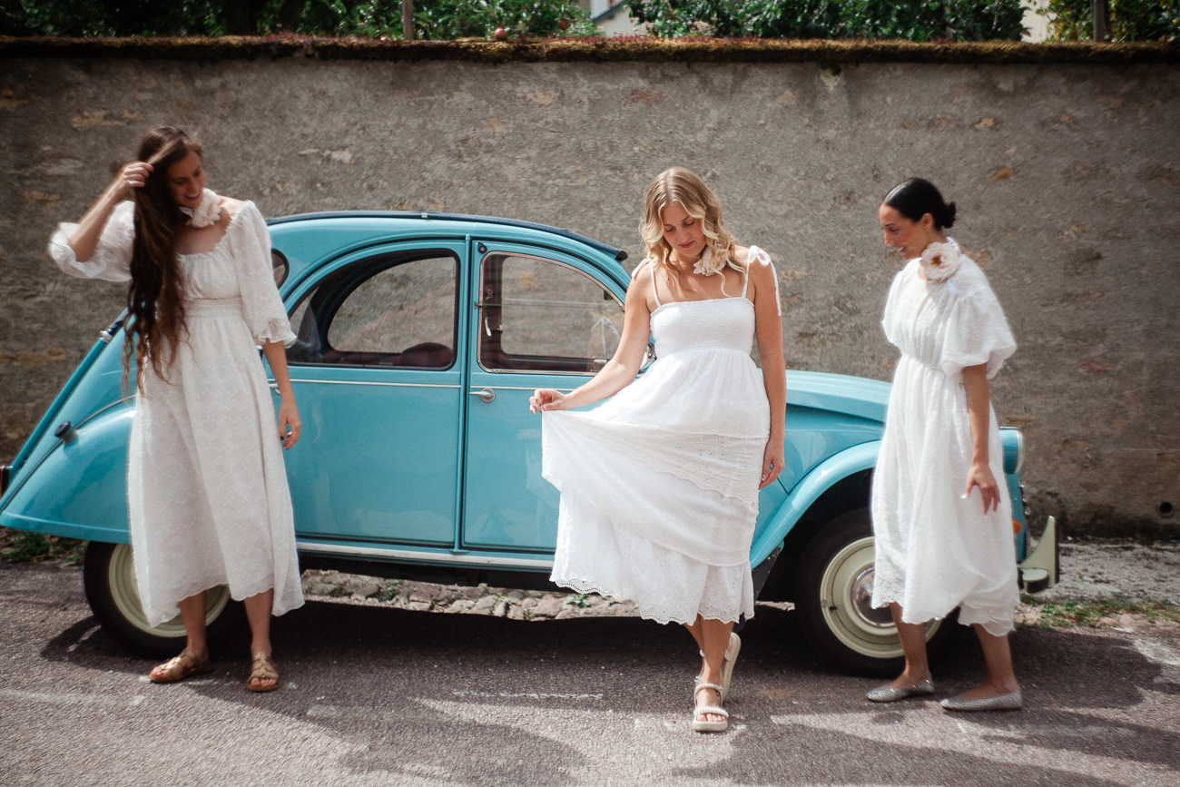three women in white dresses in front of a blue car