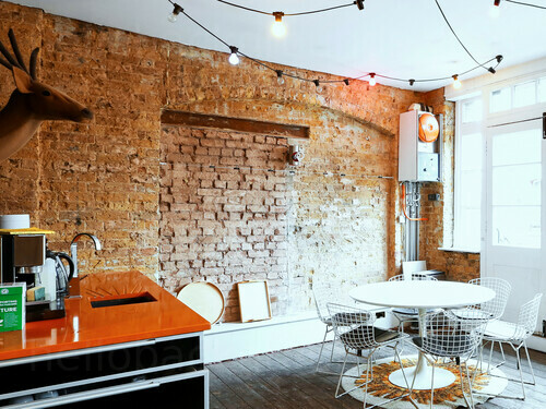 Intimate meeting space with bare brick walls and wooden flooring containing small round white table and coffee station  Google Meet background