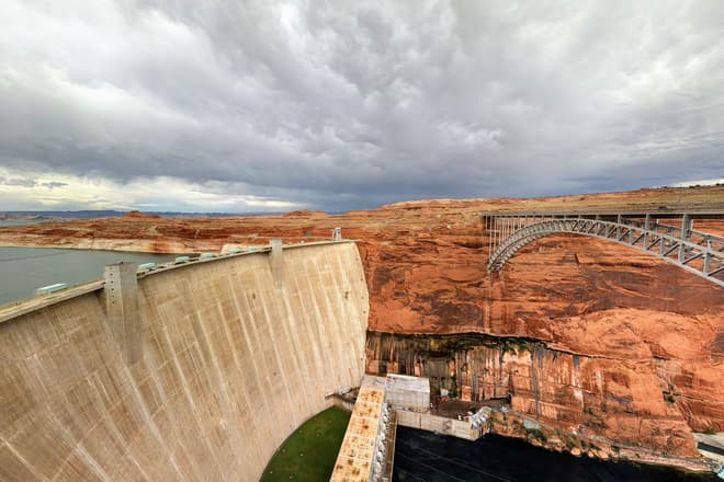 A wide-angle shot of the Glen Canyon Dam (left) and Glen Canyon Dam Bridge (right), with the Colorado River below.