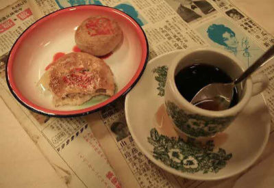 A cup of black coffee on a saucer and a plate of Chinese pastries lie on newspaper.