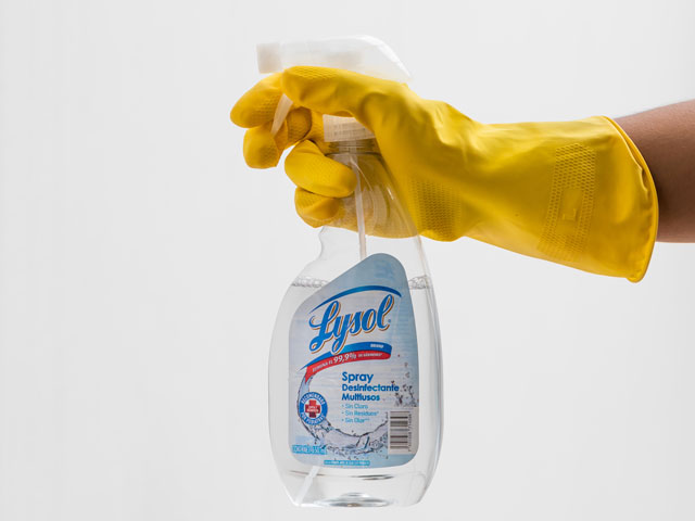 A rubber-gloved hand holding a bottle of Lysol spray disinfectant