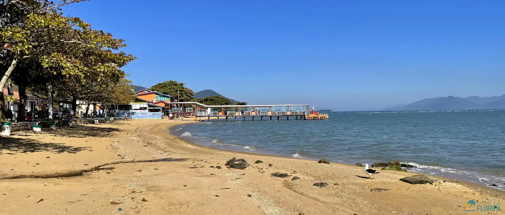 Vista da pequena faixa de areia com trapiche/restaurante característico da região.