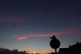 Wispy pink clouds against a dark blue sky with a silhouette of a street sign in the foreground.