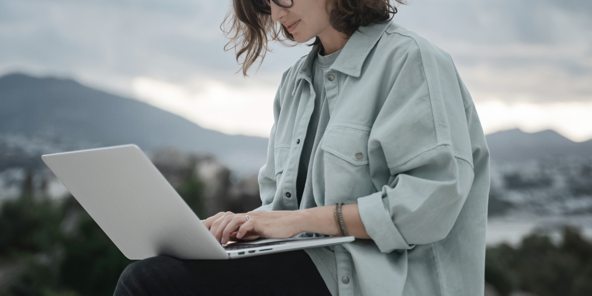 Is it possible to work as a remote UI designer? A user interface designer sitting against a mountainous background, typing on a laptop