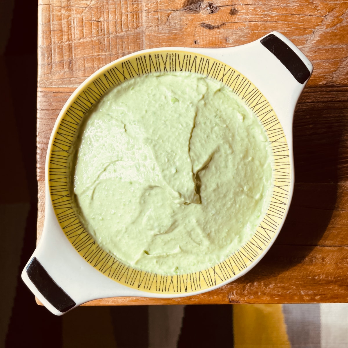 A pale, greenish-yellow dip in a bowl on a wooden table.