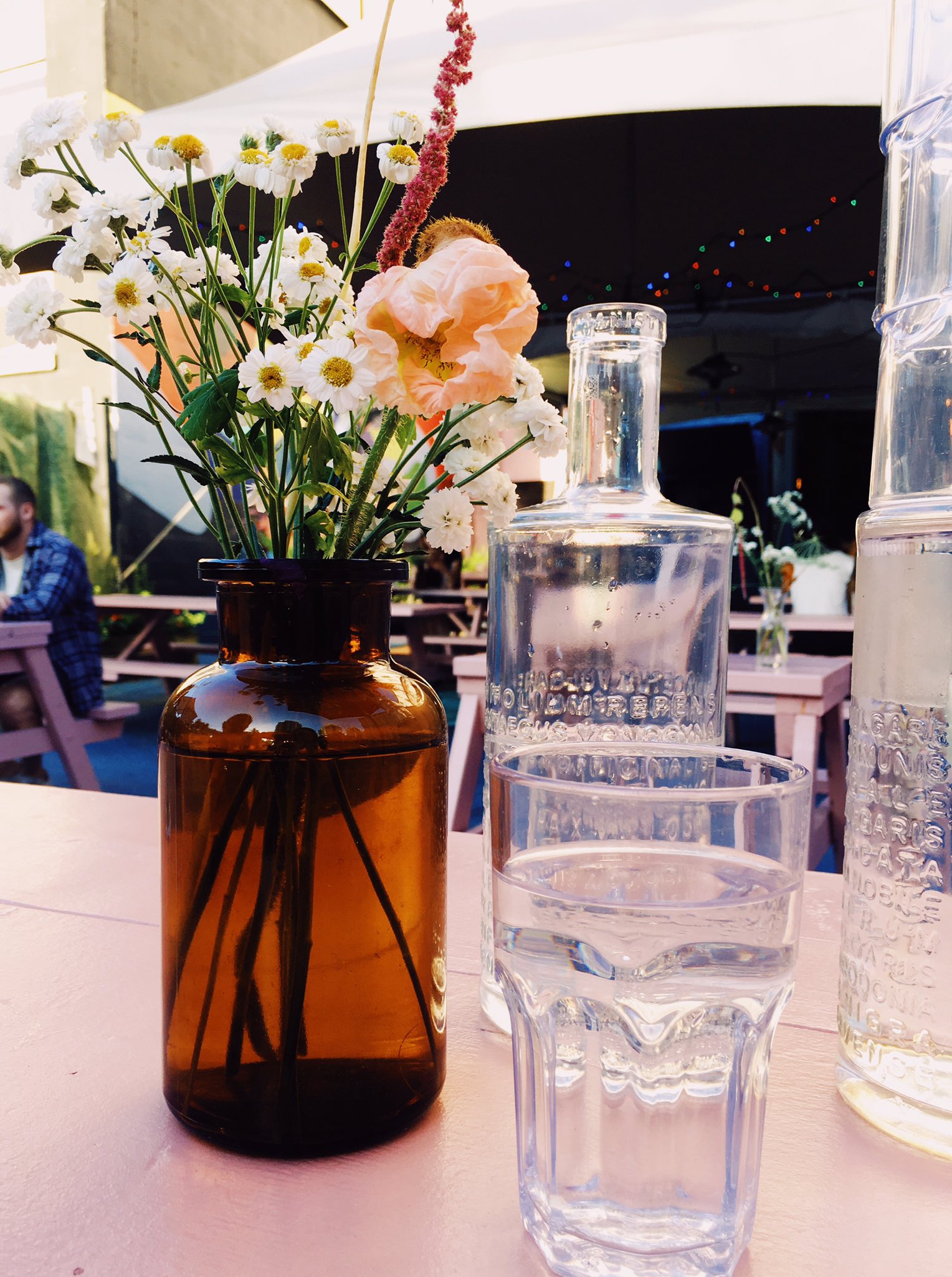 A vase of flowers and glasses of water on an pink picnic table, on a lovely summer evening.