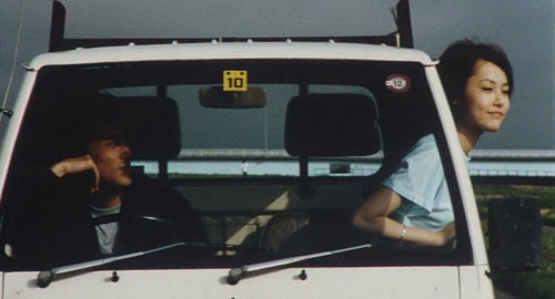 From the film 'Hole in the Sky'. A screenshot of a man driving a truck while in the passenger seat a woman (played by Rink Kikuchi) sticks her head out of the window.