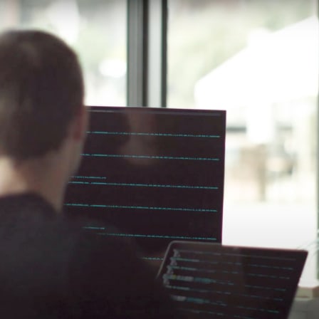 Back of a mans head looking towards 2 screens.