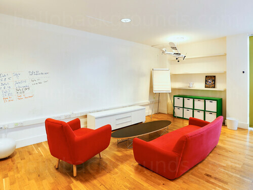 Simplistic white walled and wooden floored meeting space with red furniture Zoom background