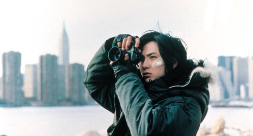 A screenshot from the movie 'Love Collage' of a guy taking a photograph with a professional camera. New York City is in the background.