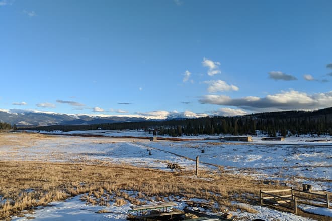 Looking out across a snowy high country ranch. In the distance, the Rocky Mountains.