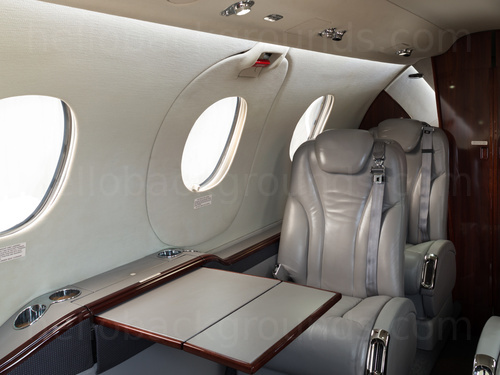 Private jet interior with gray leather seats and folded out tray table Google Meet background