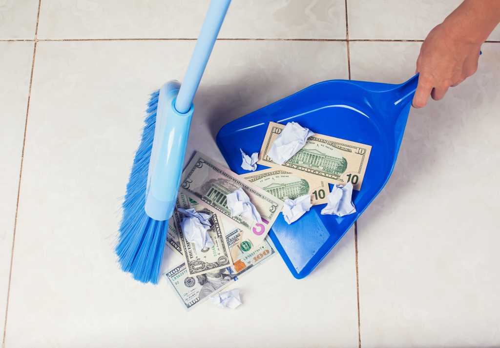 broom sweeping cash money in American bills into a blue dustpan