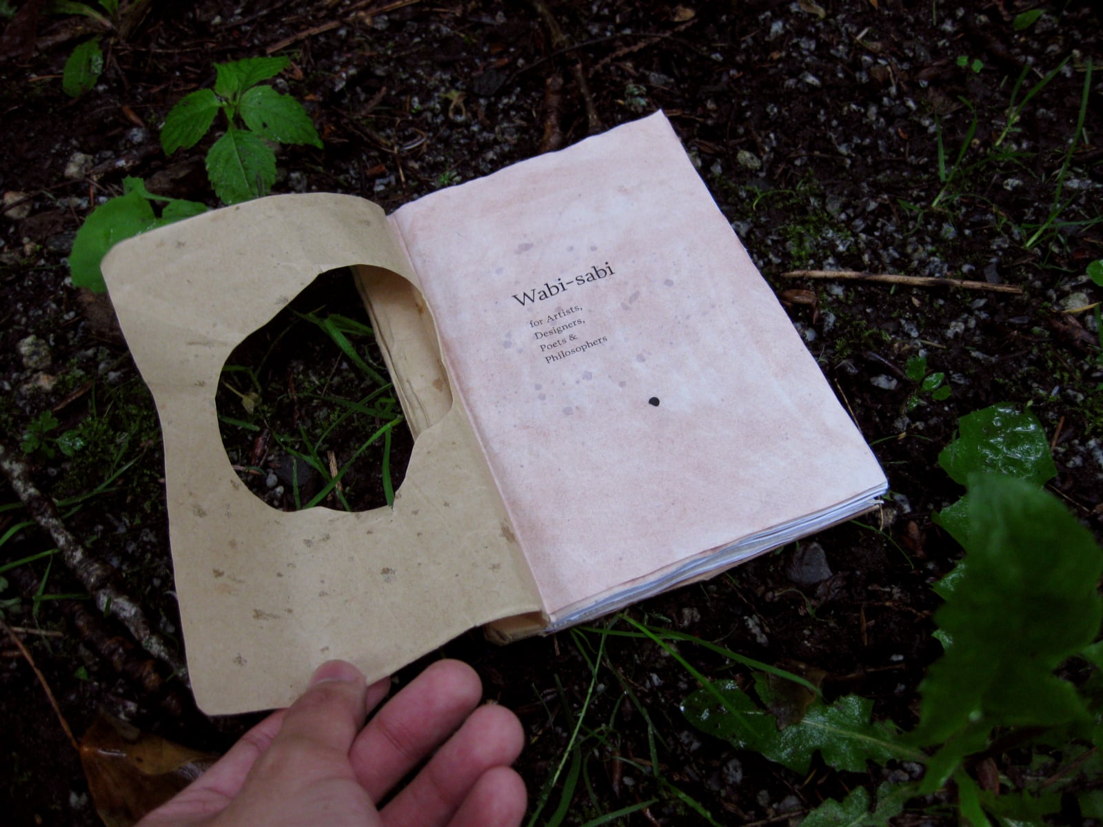 an open book on a wet forest floor. The first page is shown which shows the book title.