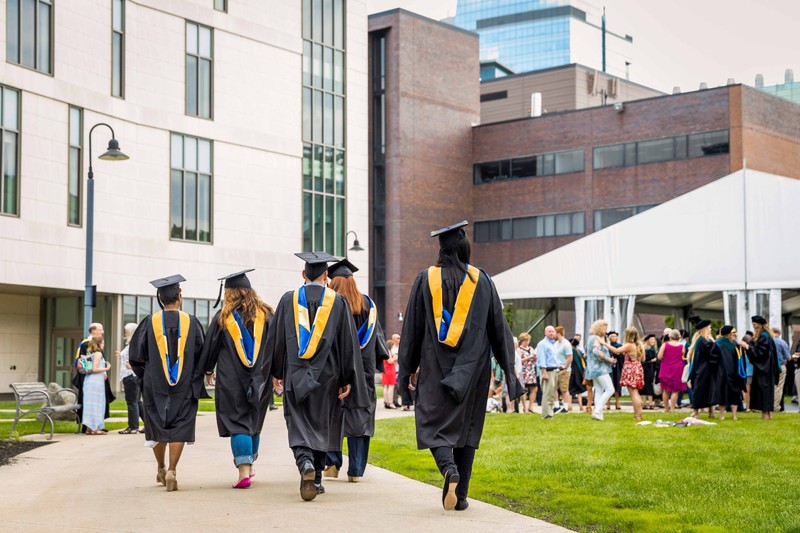 Recently graduated students in their caps and gowns walk toward a reception
