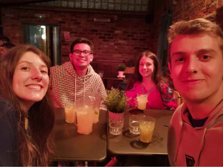 Myself, Naomi and my friends James and Siobhan sat around a table holding a variety of different coloured cocktails. This was taken after completing an escape room for my birthday. Asa result, we're wearing stickers that say, We excaped!
