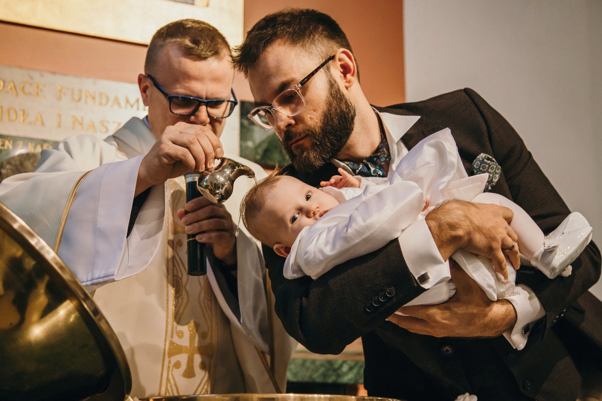 Sesja chrztu Poznań - Ojciec trzyma dziewczynkę nad chrzścielnicą