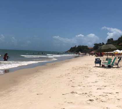 Praia a esquerda e faixa de area a direita. Guarda sol e bar bem ao fundo.