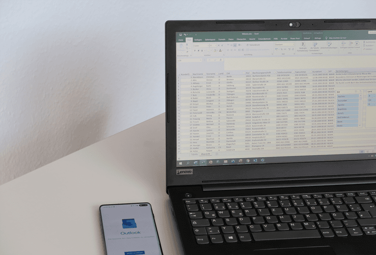 Smartphone mit Outlook-App neben einem Laptop