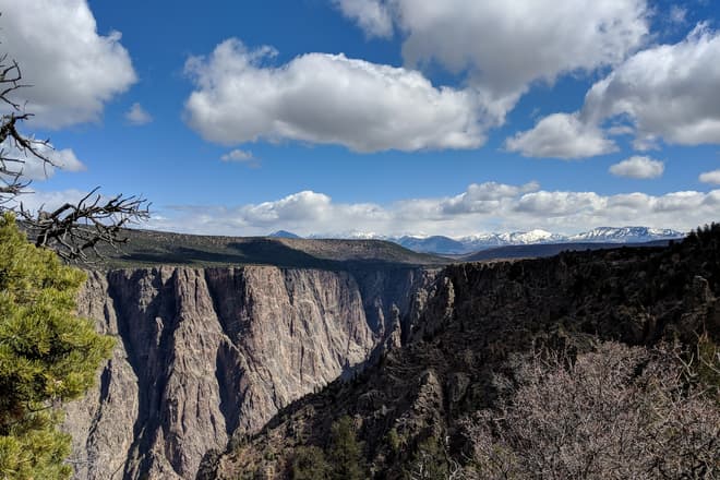 Looking northeast into the steep walls of the Black Canyon of he Gunnison. In the distance, a range of domed, snow-covered peaks.
