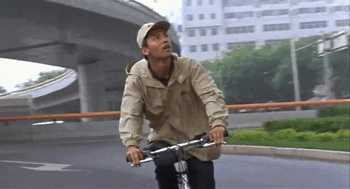 An animated gif of a scene from the movie 'Beijing Bicycle' of a young man excitedly peddling his bicycle in traffic.